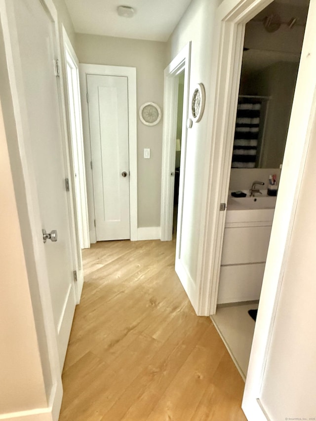 corridor featuring baseboards, light wood-style floors, and a sink