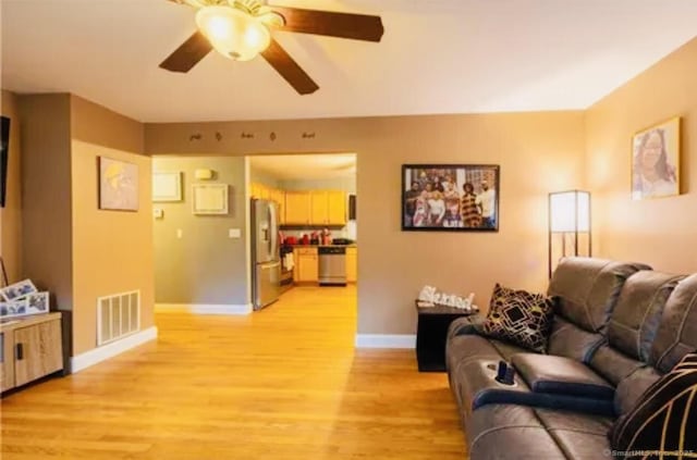 living room with a ceiling fan, light wood-style floors, visible vents, and baseboards