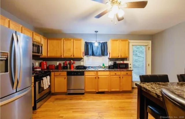 kitchen with decorative light fixtures, light wood-type flooring, a ceiling fan, dark countertops, and appliances with stainless steel finishes
