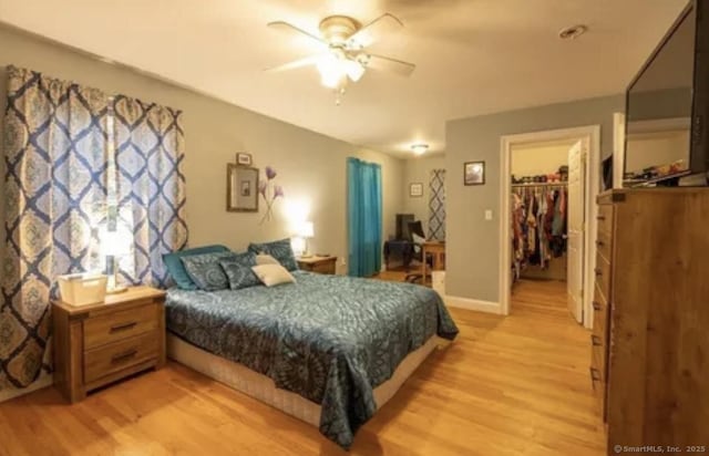 bedroom with baseboards, light wood finished floors, a closet, and a walk in closet