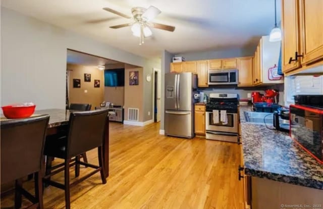 kitchen featuring light wood finished floors, a ceiling fan, dark countertops, visible vents, and appliances with stainless steel finishes
