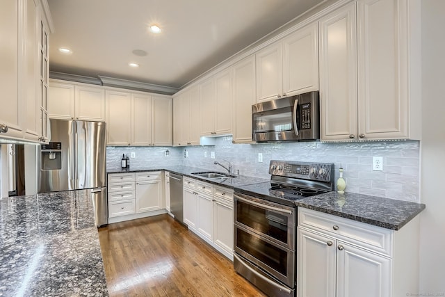 kitchen with appliances with stainless steel finishes, a sink, tasteful backsplash, dark stone countertops, and dark wood-style floors