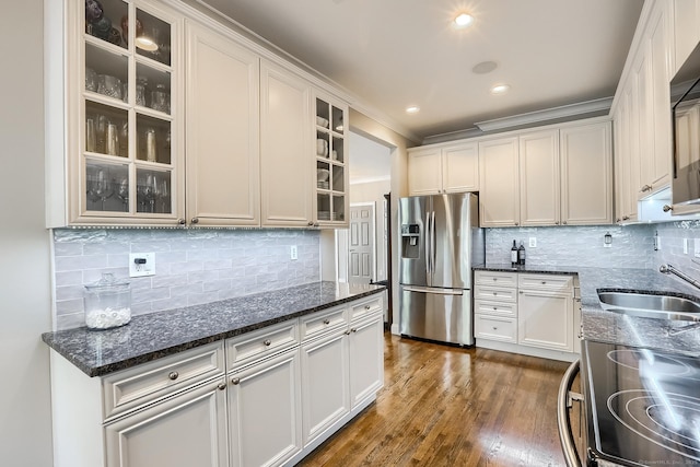 kitchen with stainless steel fridge with ice dispenser, a sink, decorative backsplash, electric range oven, and dark stone counters