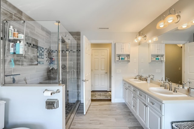 bathroom featuring wood finished floors, a stall shower, double vanity, and baseboards
