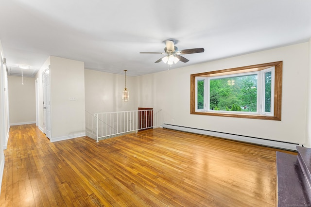 empty room with attic access, a baseboard heating unit, a ceiling fan, hardwood / wood-style floors, and baseboards