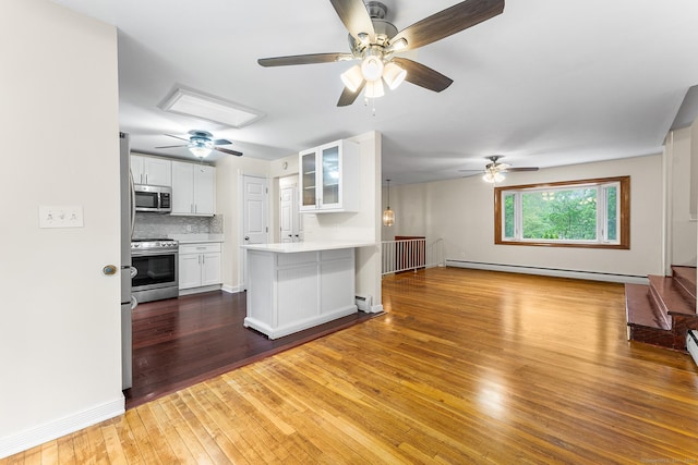 kitchen featuring appliances with stainless steel finishes, open floor plan, a baseboard radiator, a ceiling fan, and glass insert cabinets