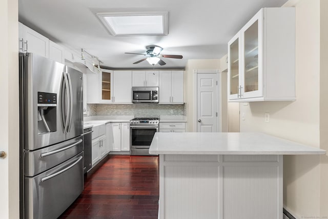 kitchen with stainless steel appliances, a peninsula, decorative backsplash, glass insert cabinets, and dark wood-style floors