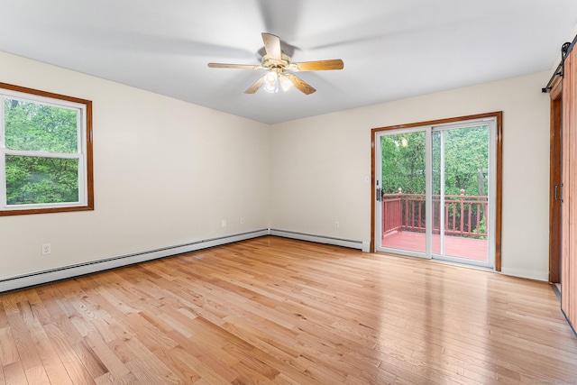 spare room featuring a barn door, a baseboard heating unit, light wood finished floors, ceiling fan, and baseboard heating