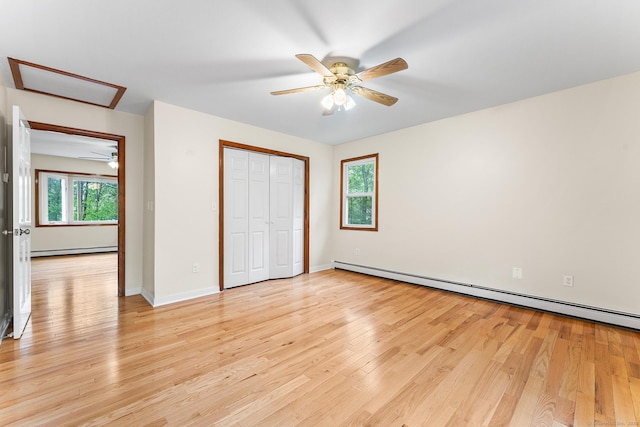 unfurnished bedroom featuring a baseboard heating unit, attic access, light wood-style floors, and baseboards