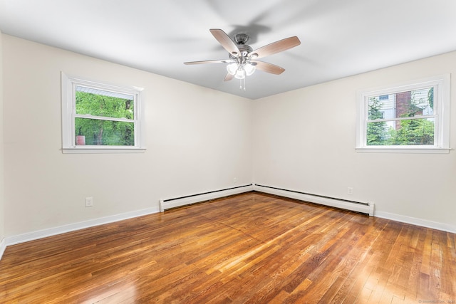 empty room featuring a baseboard heating unit, plenty of natural light, and hardwood / wood-style flooring