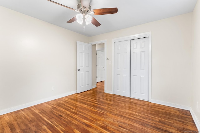 unfurnished bedroom featuring baseboards, wood finished floors, a closet, and a ceiling fan