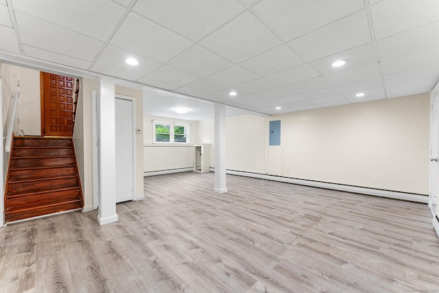 basement featuring light wood finished floors, a baseboard heating unit, electric panel, baseboards, and a drop ceiling