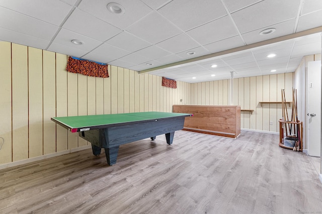 game room featuring a drop ceiling, wood finished floors, baseboards, and wooden walls