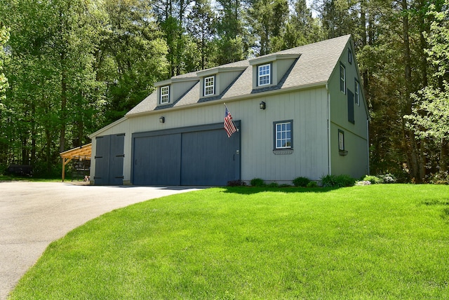 view of front facade featuring roof with shingles, a front lawn, driveway, an attached garage, and view of wooded area