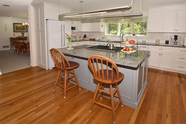 kitchen with white appliances, white cabinets, tasteful backsplash, and wood finished floors