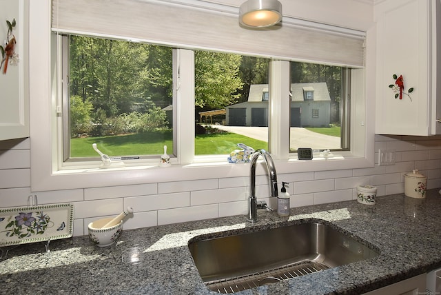 kitchen featuring a sink, tasteful backsplash, white cabinetry, and dark stone countertops