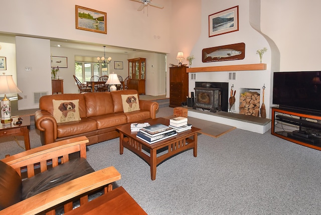 carpeted living area with a chandelier, a wood stove, ceiling fan, and a towering ceiling