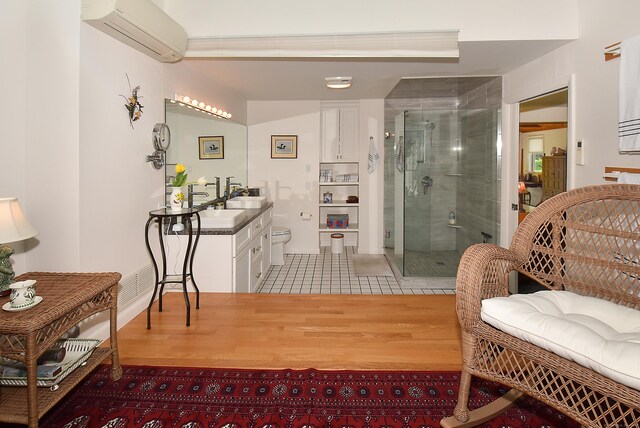 bathroom featuring a shower stall, an AC wall unit, wood finished floors, toilet, and vanity