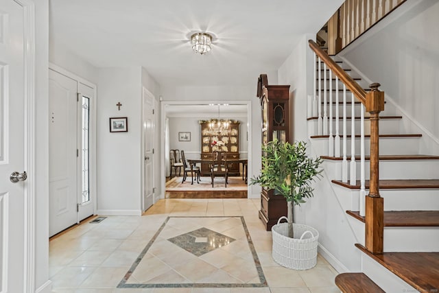 entryway with inlaid floor details, a chandelier, stairway, baseboards, and light tile patterned floors