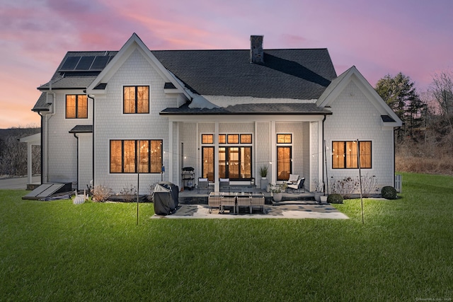 100 Georgetown Rd, Weston, CT 06883 - back of house at dusk with a patio, a lawn, roof mounted solar panels, roof with shingles, and a chimney