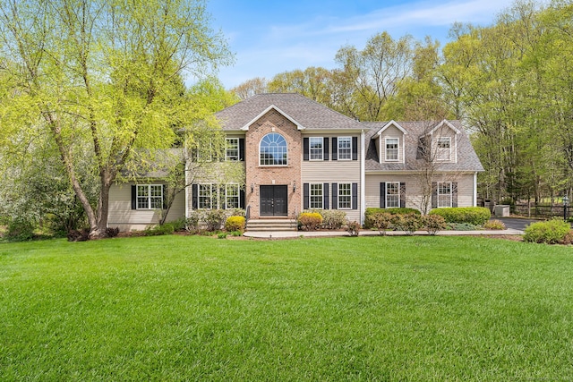 colonial-style house featuring a front yard, a shingled roof, and brick siding