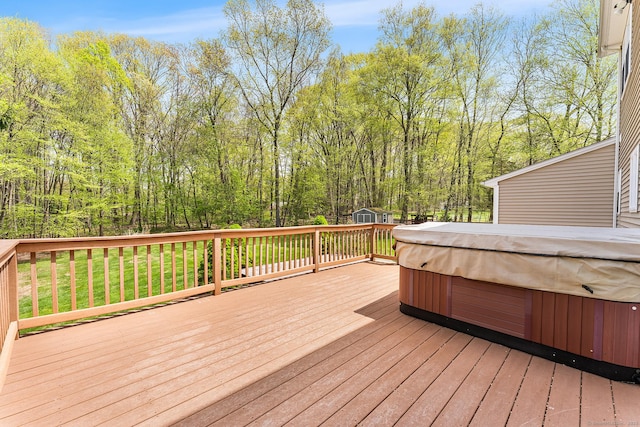 wooden terrace featuring a hot tub, a storage shed, an outdoor structure, and a view of trees