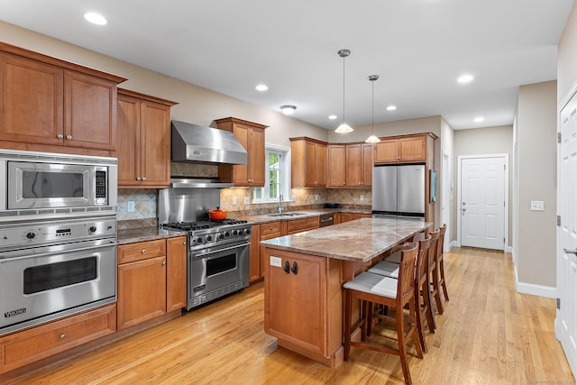 kitchen featuring appliances with stainless steel finishes, brown cabinetry, dark stone countertops, a sink, and recessed lighting