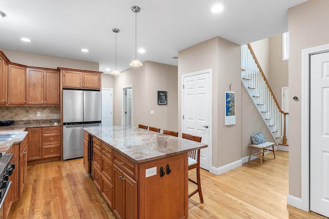 kitchen with freestanding refrigerator, brown cabinetry, light wood finished floors, a kitchen breakfast bar, and recessed lighting
