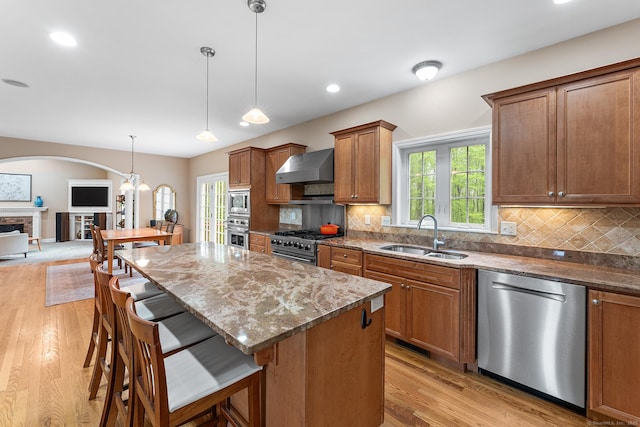 kitchen featuring a sink, stainless steel appliances, wall chimney range hood, dark stone countertops, and arched walkways