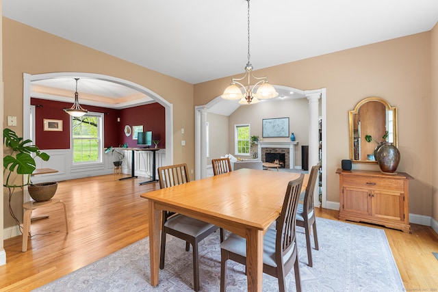 dining area with light wood finished floors, ornate columns, arched walkways, and a lit fireplace