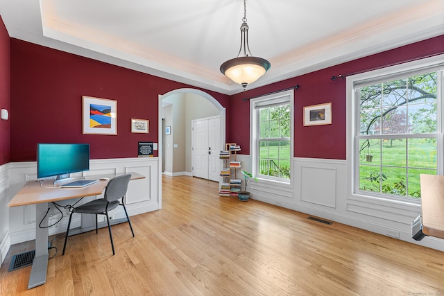 office area featuring arched walkways, wainscoting, wood finished floors, a raised ceiling, and a decorative wall