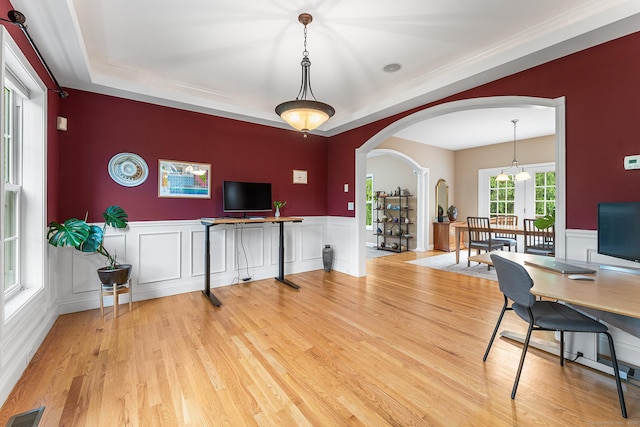 office area with arched walkways, light wood finished floors, a chandelier, a decorative wall, and a wainscoted wall