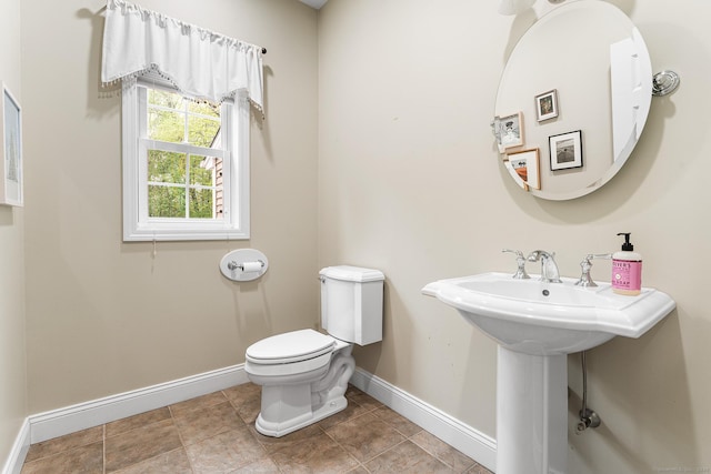 half bath with baseboards, toilet, and tile patterned floors