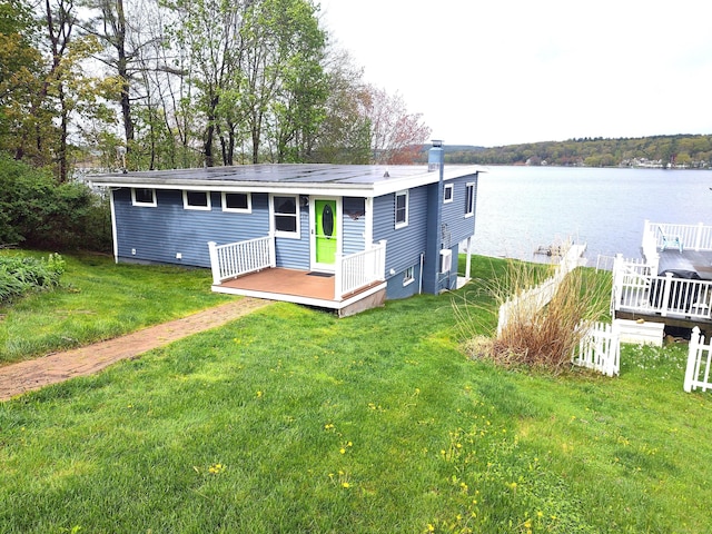 rear view of house with a deck with water view and a lawn