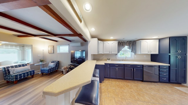 kitchen featuring dishwashing machine, light countertops, a peninsula, white cabinetry, and beamed ceiling