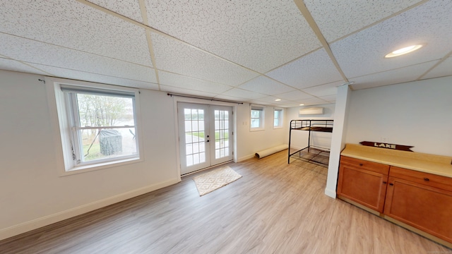 basement featuring french doors, light wood-style floors, baseboards, a drop ceiling, and recessed lighting
