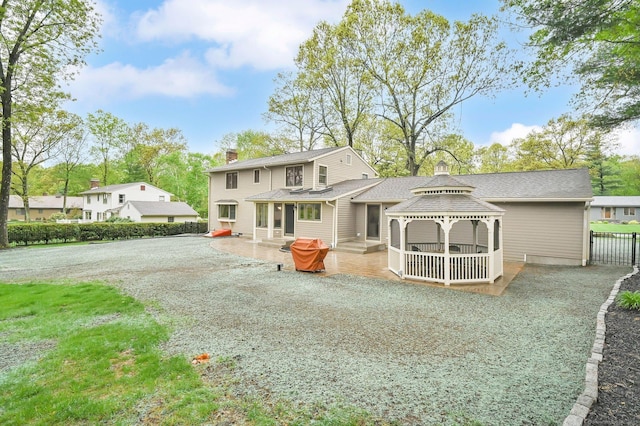 back of house with a gazebo, gravel driveway, fence, a chimney, and a patio area
