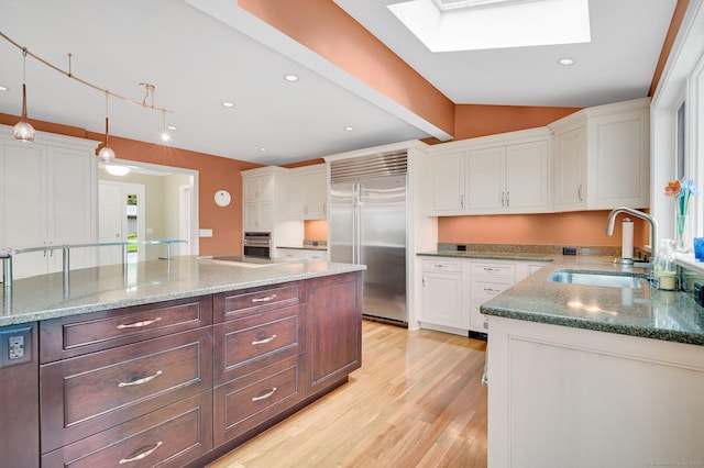 kitchen featuring appliances with stainless steel finishes, a sink, a skylight, white cabinets, and light wood-type flooring