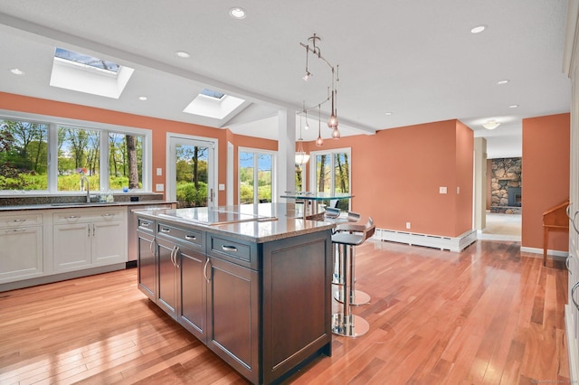 kitchen with a skylight, a sink, baseboard heating, black electric stovetop, and a breakfast bar