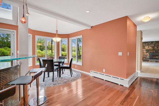 dining space featuring wood finished floors, a baseboard heating unit, baseboards, a fireplace, and beam ceiling