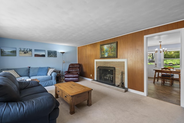 living area featuring a chandelier, a fireplace, wooden walls, baseboards, and carpet flooring