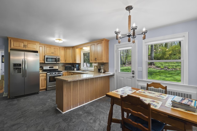 kitchen with appliances with stainless steel finishes, a peninsula, a chandelier, decorative backsplash, and a sink