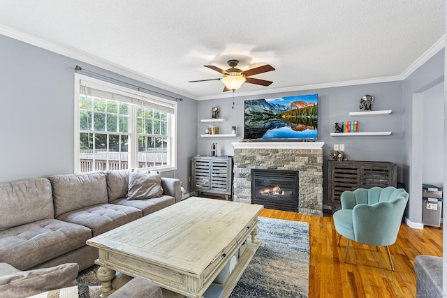living room featuring crown molding, ceiling fan, a textured ceiling, a fireplace, and wood finished floors
