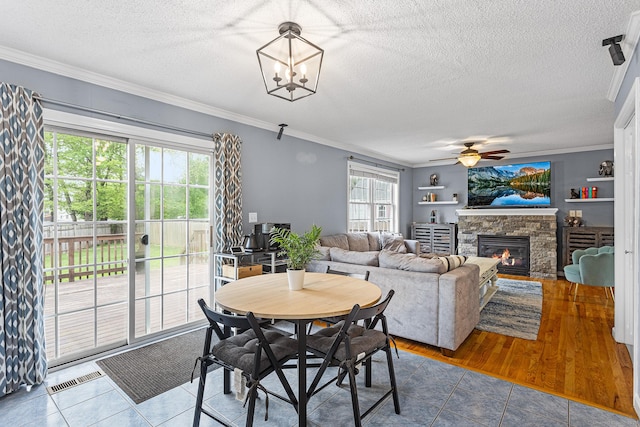 tiled dining space with crown molding, a textured ceiling, a ceiling fan, a fireplace, and a chandelier