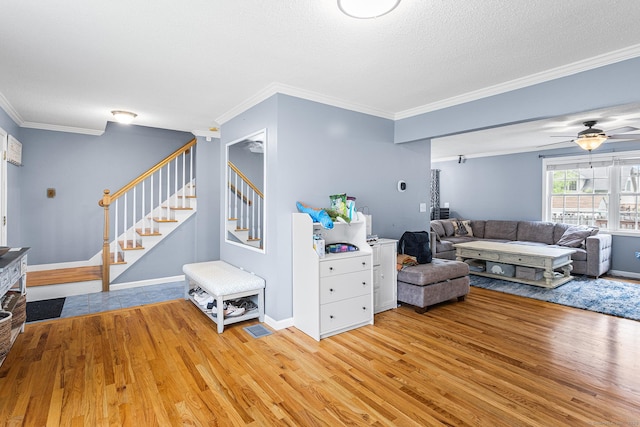 living area with light wood-style flooring, stairway, crown molding, a textured ceiling, and a ceiling fan