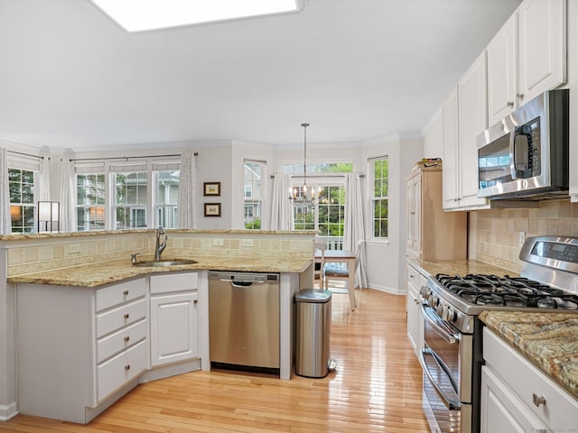 kitchen with stainless steel appliances, a sink, crown molding, a chandelier, and baseboards