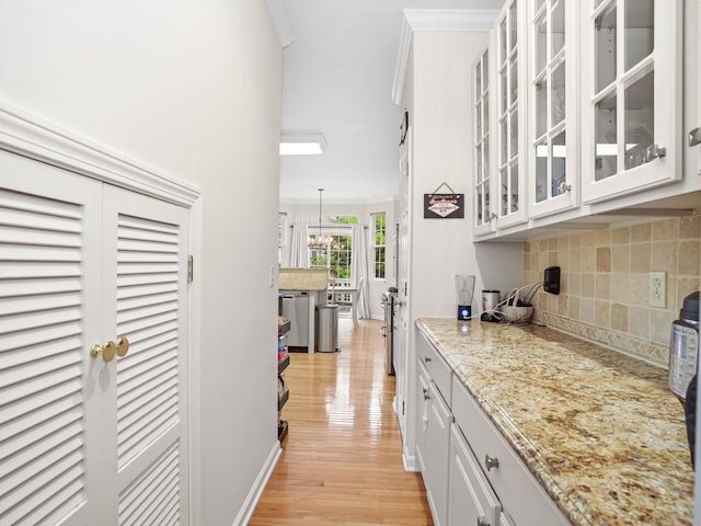 bar area with backsplash, ornamental molding, light wood-style floors, a chandelier, and stainless steel dishwasher