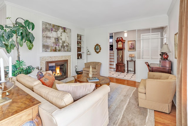 living area with wood finished floors, a glass covered fireplace, crown molding, built in features, and baseboards