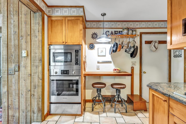 kitchen featuring a warming drawer, stainless steel microwave, light tile patterned flooring, decorative light fixtures, and brown cabinets