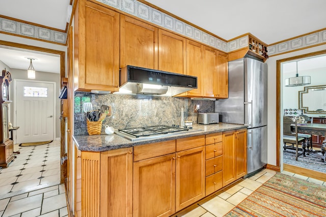 kitchen featuring stainless steel appliances, tasteful backsplash, under cabinet range hood, brown cabinets, and dark stone countertops